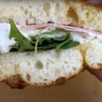 Close-up of a fresh sandwich with arugula, ham, cheese, and rustic bread, perfect for a quick, delicious meal.